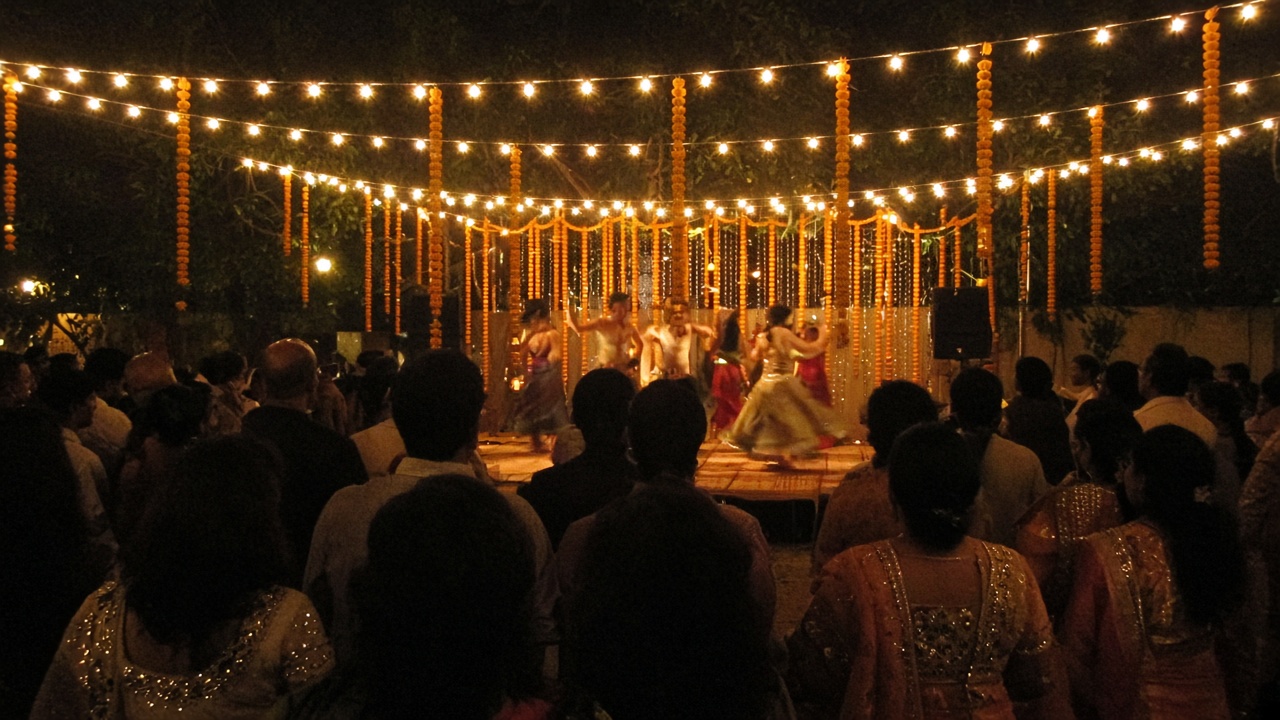 Guests seen from behind watching a performance on a lit sangeet stage